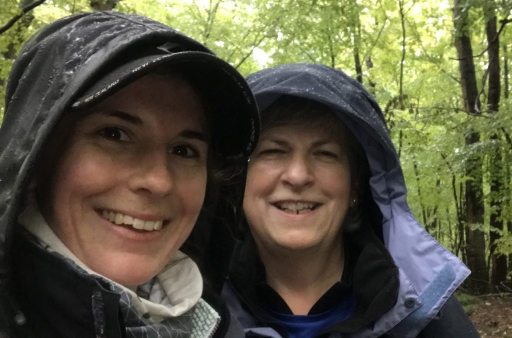 Close up of Jocelyn and Vanessa smiling to camera wearing damp rain hoods