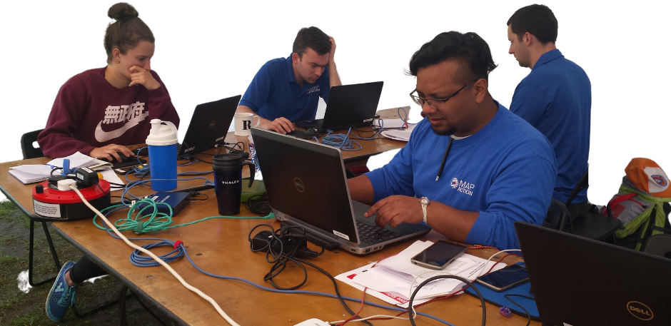 Four MapAction volunteers working with great concentration at individual laptops under canvas